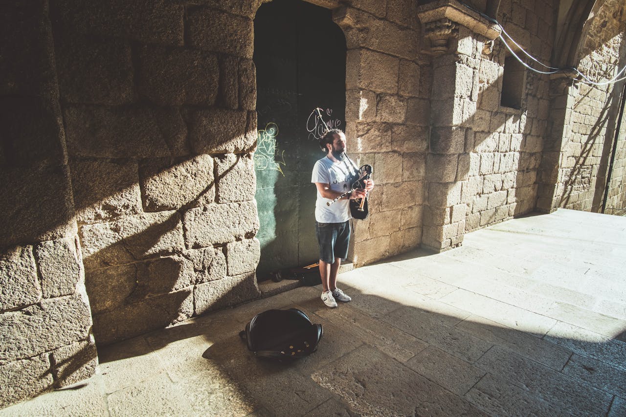 A street musician playing bagpipes by a historic stone facade in Santiago de Compostela, Spain.